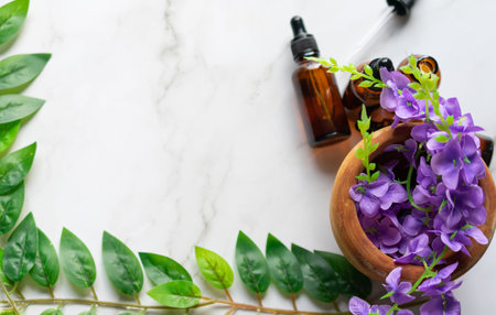 A mortar with some purple flowers and some amber vials of essential oils on a white marble surfaceの写真素材