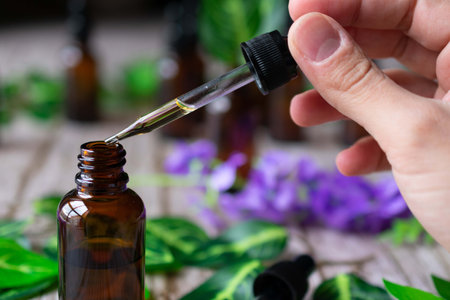 Close-up of a hand taking some essential oil from an amber vial with a dropper. Some leaves and flowers in the backgroundの写真素材