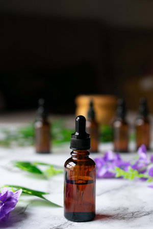 Several amber vials of essential oil on a marble surface, with flowers and leaves around them, and a candle on the background.の写真素材