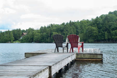 Two empty chairs on a deck over a lakeの写真素材