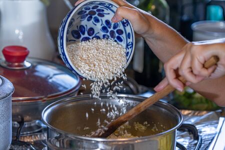 Pouring a rice bowl into the pan for a zucchini risotto preparation. With hot water and seasoned with salt and garlic.の写真素材