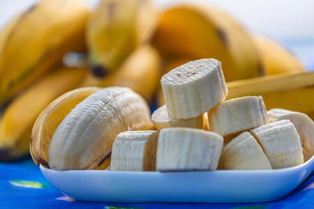 A bunch of bananas and sliced bananas on a blue tablecloth background. Served on a small square plate, very ripe and fresh.の写真素材