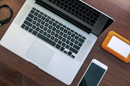 View of the black screen of the laptop, a device to work at home, do research, agenda, HD, cell phone and USB drive. On top of a wooden office table.の写真素材