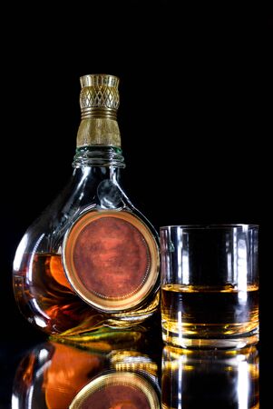 An imposing and beautiful bottle of whiskey on black background. Layout with free text space and a glass served with whiskey.の写真素材