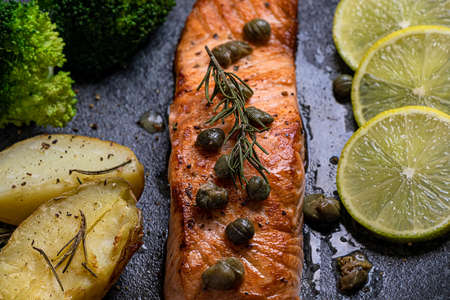 A piece of roasted salmon grilled lemon pepper and salt on a dark plate with broccoli. Wood...