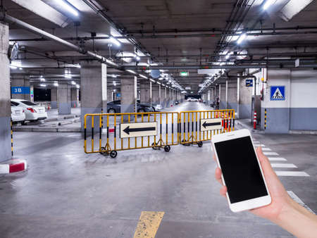Hand holding mobile phone with indoor parking lot building. Social network, internet conceptの写真素材