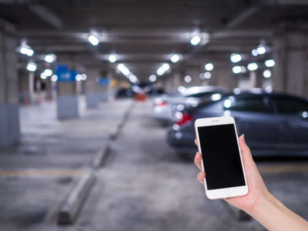 Hand holding mobile phone with indoor parking lot building blurred background and bokeh light, Social network, internetの写真素材
