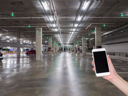 Hand holding mobile phone with indoor parking lot building blurred background and bokeh light, Social network, internetの写真素材