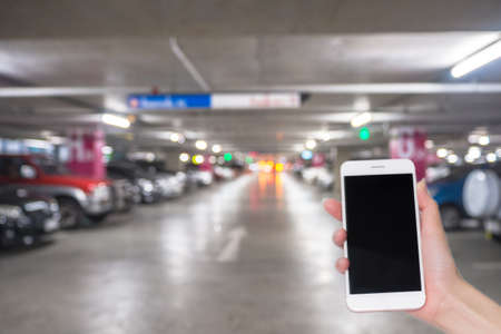 Hand holding mobile phone with indoor parking lot building. Social network, internet conceptの写真素材