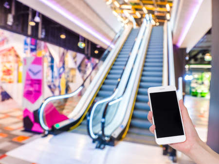 Hand holding mobile phone with Shopping mall or department store blurred background and bokeh light,...