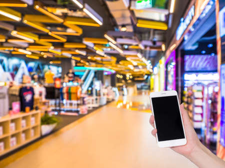 Hand holding mobile phone with Shopping mall or department store blurred background and bokeh light, Social network, internetの写真素材