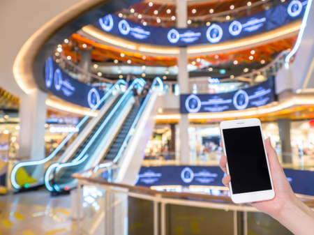 Hand holding mobile phone with Shopping mall or department store blurred background and bokeh light, Social network, internetの写真素材