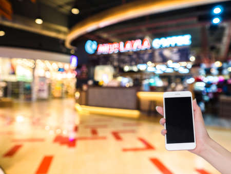 Hand holding mobile phone with Shopping mall or department store blurred background and bokeh light,...