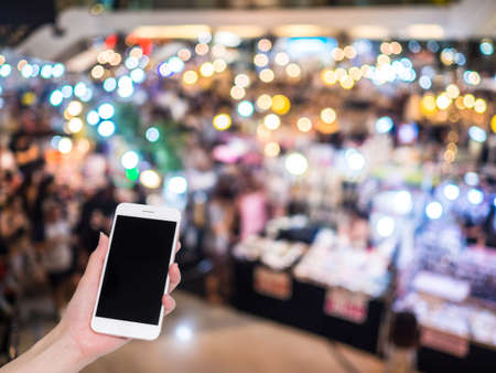 Hand holding mobile phone with Shopping mall or department store blurred background and bokeh light, Social network, internetの写真素材