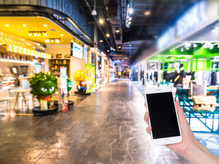 Hand holding mobile phone with Shopping mall or department store blurred background and bokeh light, Social network, internetの写真素材