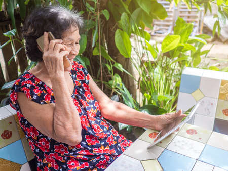 Smiling elderly woman while talking mobile phone sitting in gardenの写真素材