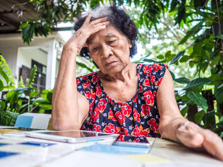 Asian senior woman unhappy while looking at mobile phone abstract loss in profits sitting in the garden, internet social media, networkの写真素材