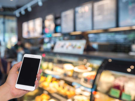 Hand holding mobile phone with blurred of coffee shop backgroundの写真素材