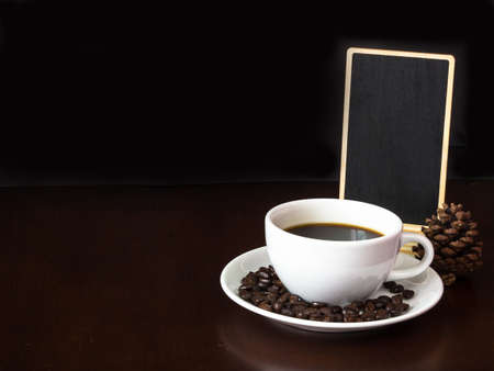 White cup coffee with coffee beans and blank chalk board on wooden top tableの写真素材