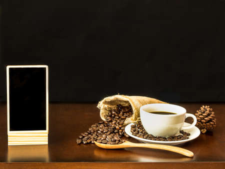 White cup coffee with coffee beans and blank chalk board on wooden top tableの写真素材