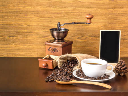 White cup coffee with coffee beans and blank chalk board on wooden top tableの写真素材