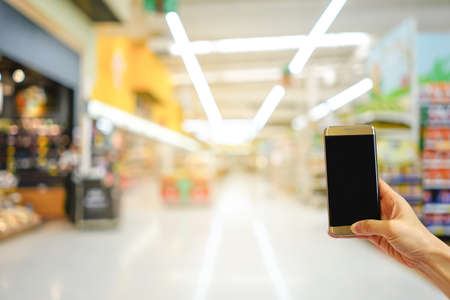 Hand holding mobile phone with shopping mall blurred background and bokeh light, Internet, Social medaiの写真素材