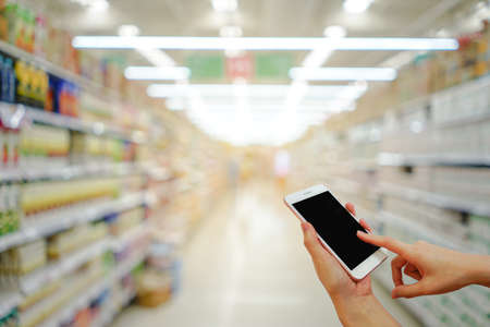 Hand holding mobile phone with shopping mall blurred background and bokeh light, Internet, Social medaiの写真素材