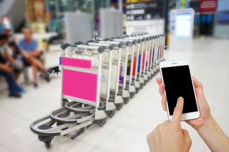 Hand holding mobile phone with airport terminal blurred crowd of Travelling people on the background, Bokeh light, Social network, internet,Traveling conceptの写真素材