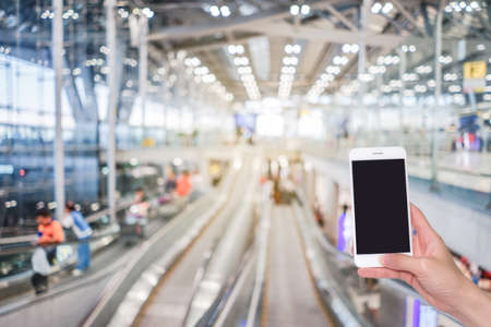 Hand holding mobile phone with airport terminal blurred crowd of Travelling people on the background, Bokeh light, Social network, internet,Traveling conceptの写真素材