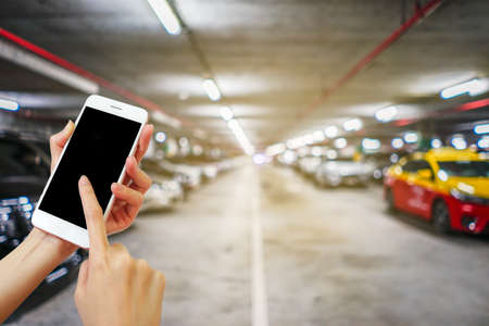 Hand holding mobile phone with blurred image of indoor car parking lot area, Internet, Social mediaの写真素材