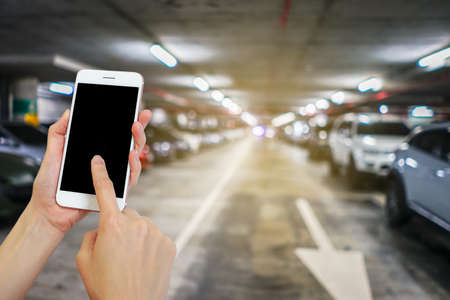 Hand holding mobile phone with blurred image of indoor car parking lot area, Internet, Social mediaの写真素材