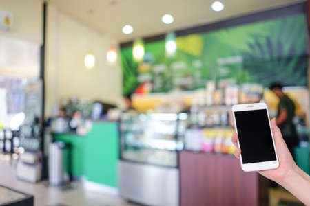 Hand holding mobile phone with blurred  coffee cafe for background usage, bokeh light, Social network, Internetの写真素材