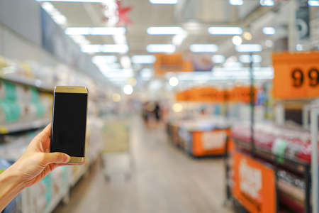 Hand holding mobile phone with shopping mall blurred background and bokeh light, Internet, Social medaiの写真素材