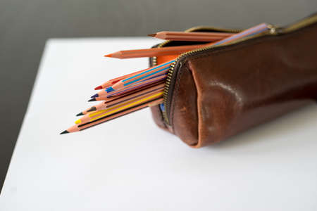 Colored pencils in pencil case on white paper and black wooden tableの写真素材