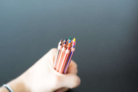 Colored pencils in hand on black wooden tableの写真素材