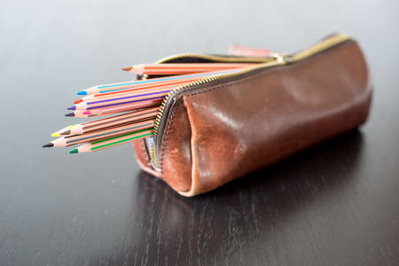 Colored pencils in pencil case on black wooden table