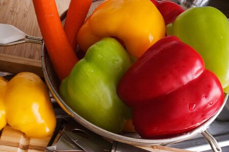 colorful bell peppers and carrots laying in colander and ready for cookingの写真素材