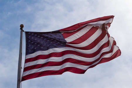 American Flag with sun shining through on windy day.