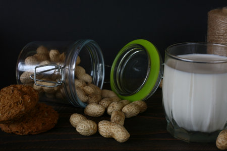 Glass jar with peanuts and glass of milk on wooden table on black background