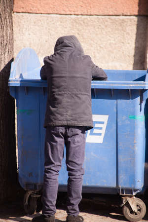 A man in a gray jacket and black pants walks through the trash can.