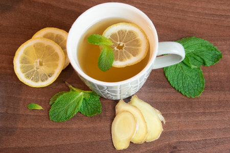 Lemon and mint float in healing tea. Ginger, mint and lemon surround mug.