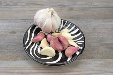 Fresh garlic head with peeled and unpeeled garlic cloves in a small ceramic bowlの写真素材