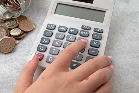 Girls fingers on calculator with jar of coins. Marble back ground copy spaceの写真素材