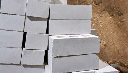 A white silicate brick is stacked, with a pile of sand in the background.