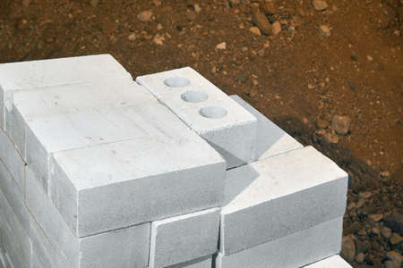 A white silicate brick is stacked, with a pile of sand in the background.