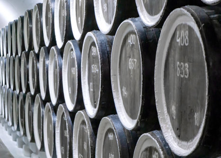 Large wooden barrels lie in the basement. Barrels for winemaking are stacked in three rows. There are inscriptions in Arabic numerals on the bottom of each barrel.の写真素材