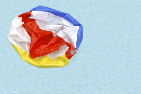 A deflated beach ball floating in a swimming pool symbolizing the end of summer.の写真素材