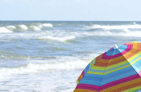 A colorful beach umbrella in foregraound with ocean waves in backgroundの写真素材