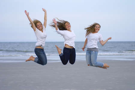 Three teenage girls jumping for joy at the beach        の写真素材