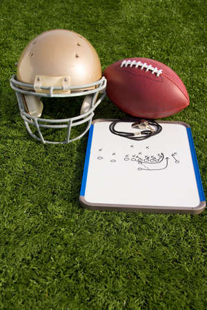A football, helmet, clipboard and whistle on an artificial turf field.